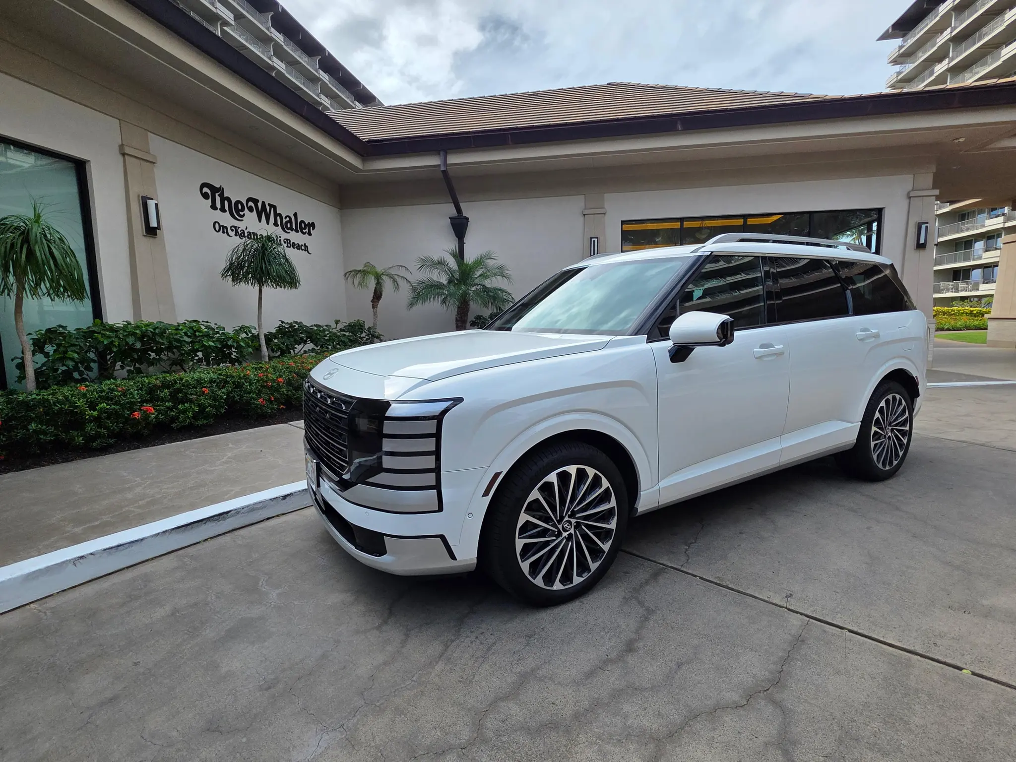 A white SUV is parked on a driveway in front of The Whaler on Kaanapali Beach building, with palm plants and a modern exterior visible.